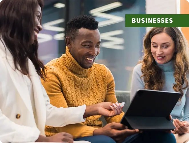 Group of three employees looking at a tablet and smiling with "business" text tag