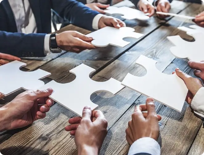 Group of employees sitting at a wooden table holding puzzle pieces together